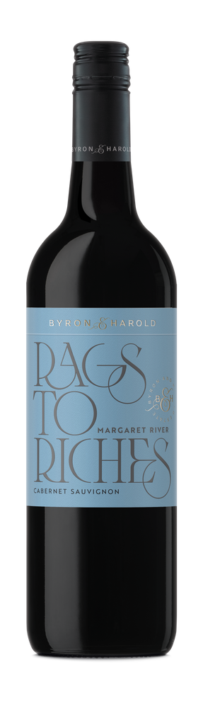 A Cabernet Sauvignon wine bottle with a black cap and dark grey label with beautiful cursive writing of Rags to Riches in light blue for Byron & Harold wines