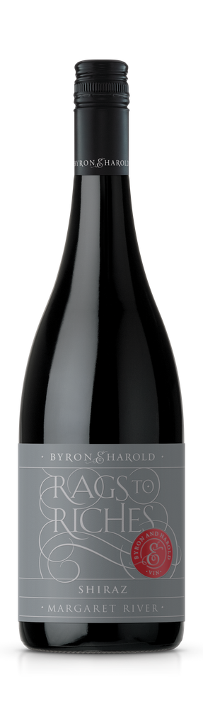 A Shiraz wine bottle with a black cap and dark grey label with beautiful cursive writing of Rags to Riches in light grey for Byron & Harold wines.